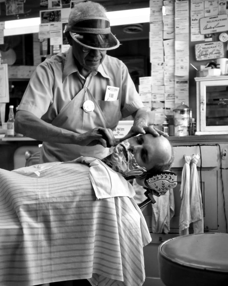 Barbero veterano atendiendo a un cliente en el sillón